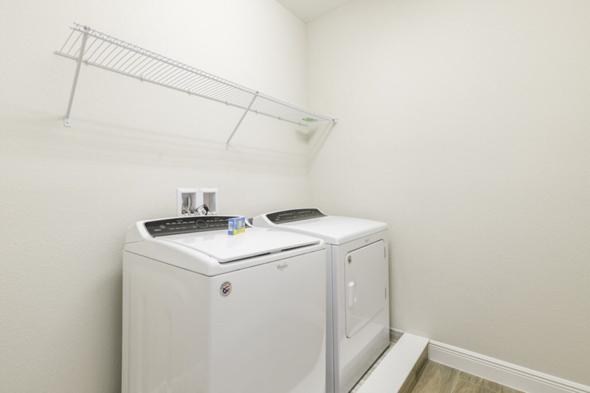 A laundry room with a front-loading washer and dryer, a metal drying rack, and a small window with a view of the outside.
