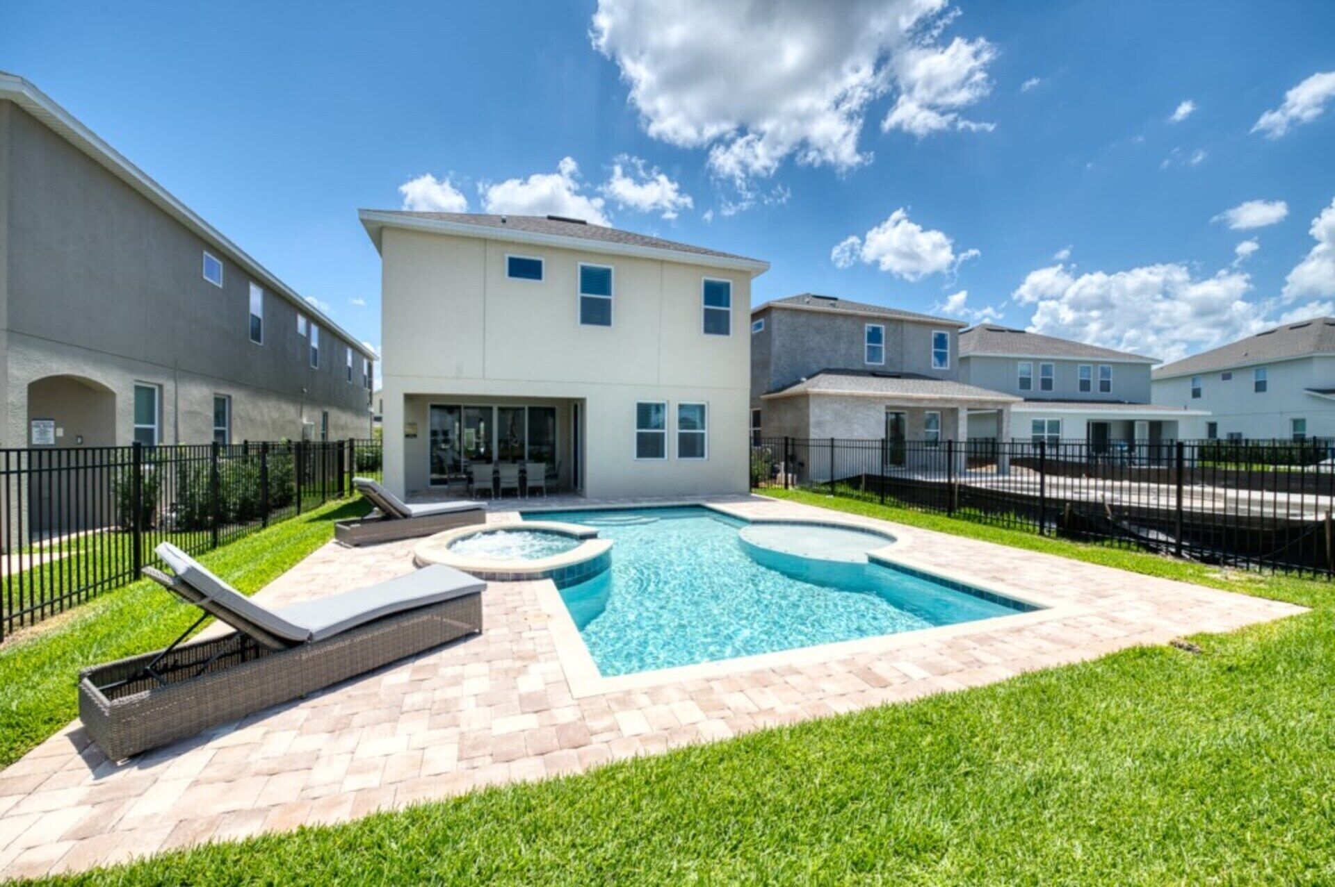 A residential area with a swimming pool, lounge chairs, and a covered patio.