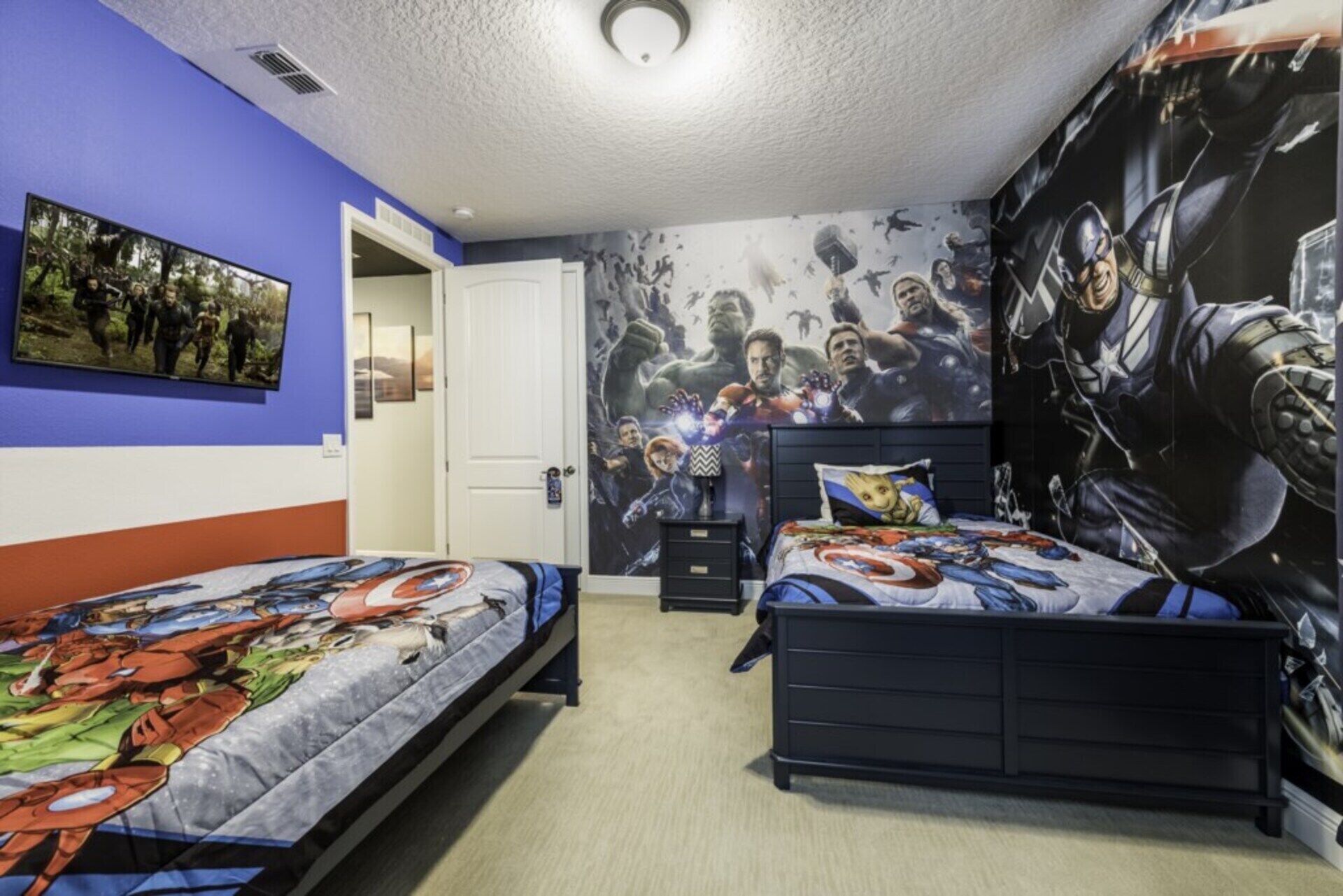 Une chambre avec deux lits, une grande fresque murale et une porte donnant sur une autre pièce.