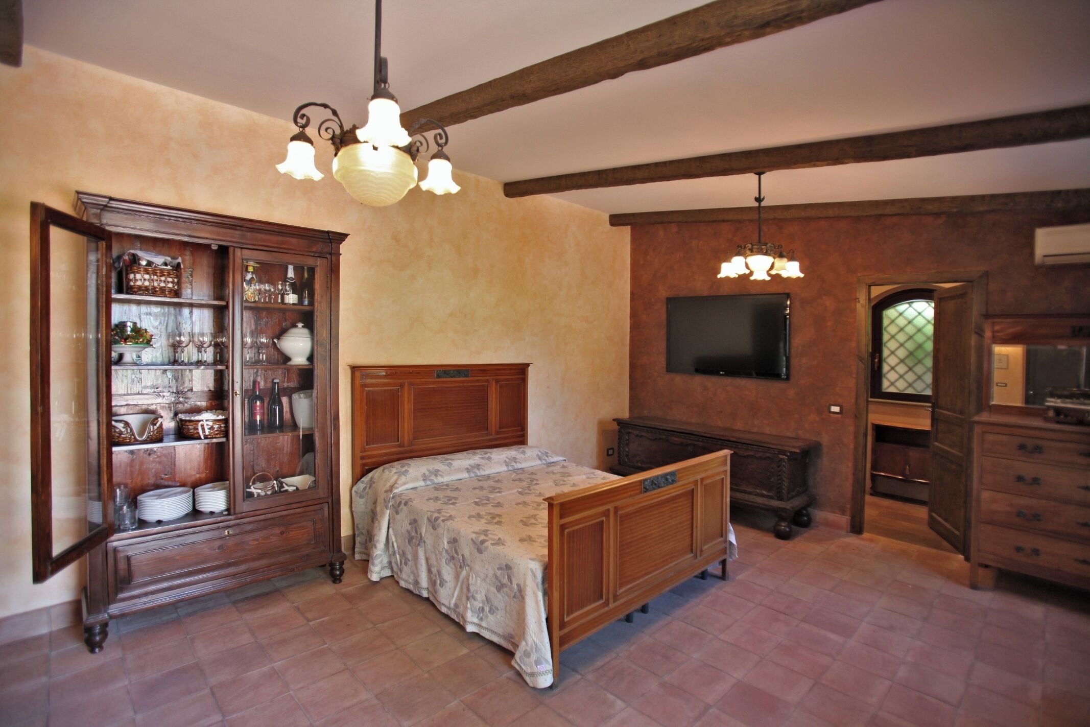 Een slaapkamer met een houten bed, een houten kast met glazen deuren, een televisie en een kroonluchter.