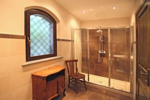 Un baño con ducha, una silla de madera, un armario y una ventana con vistas.