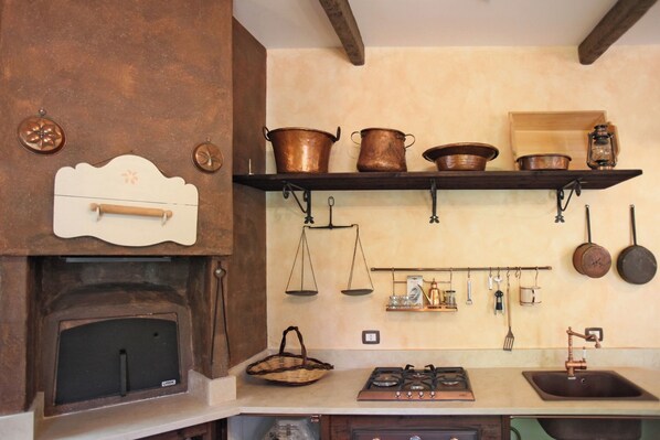 Una cocina con estufa de leña, ollas de cobre, una balanza colgante y una cocina a gas.