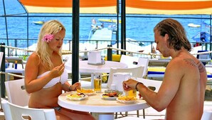 Two people dining at an outdoor table with a view of the sea and boats. - Noxinn Club Hotel  (Alanya)