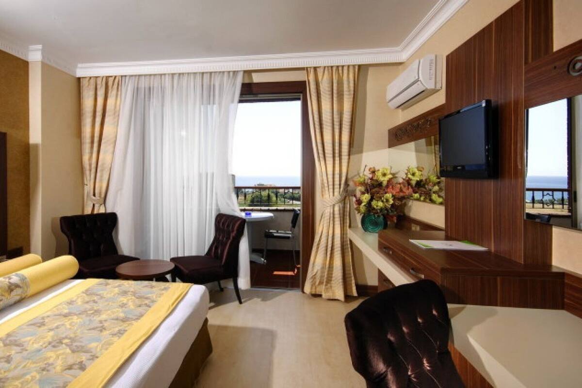 A hotel room with a bed, a desk, a chair, a TV, and a balcony with a view.