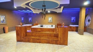 A spa area with a central hot tub, wooden benches, and a brick wall backdrop. - Noxinn Club Hotel  (Alanya)