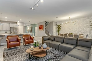 Un salon moderne avec un canapé d’angle, des fauteuils en cuir, une table basse et un tapis à motifs.