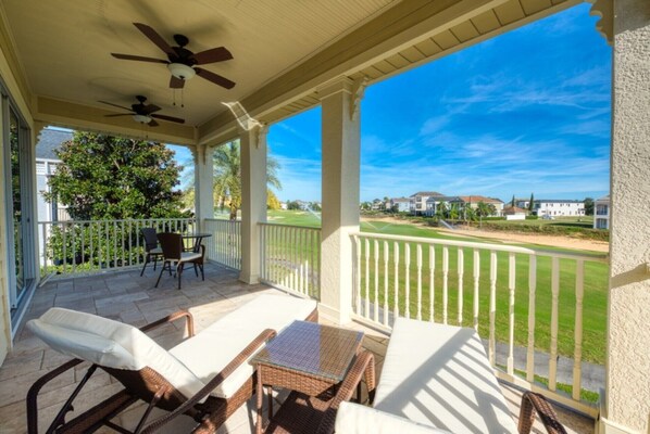 A covered patio with outdoor furniture, a ceiling fan, and a view of a golf course and residential area.