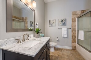 A bathroom with a marble sink, a toilet, a shower with glass doors, and artwork on the walls.