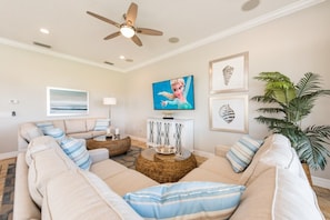 A living room with a beige sofa, a round coffee table, a ceiling fan, and a television.