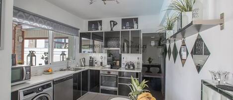 A modern kitchen with a built-in washer, a dining area with a fruit bowl, and a view of the street.