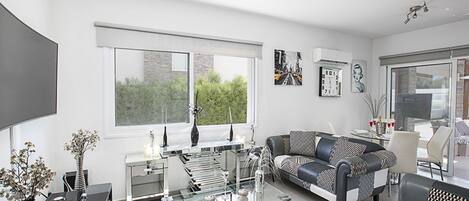 A modern living room with a glass coffee table, a black and white patterned sofa, and a dining area with a glass table and chairs.