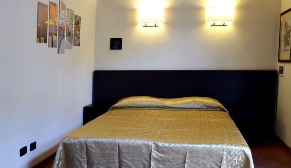 A hotel room with a bed, two wall-mounted lights, and a series of paintings on the wall.
