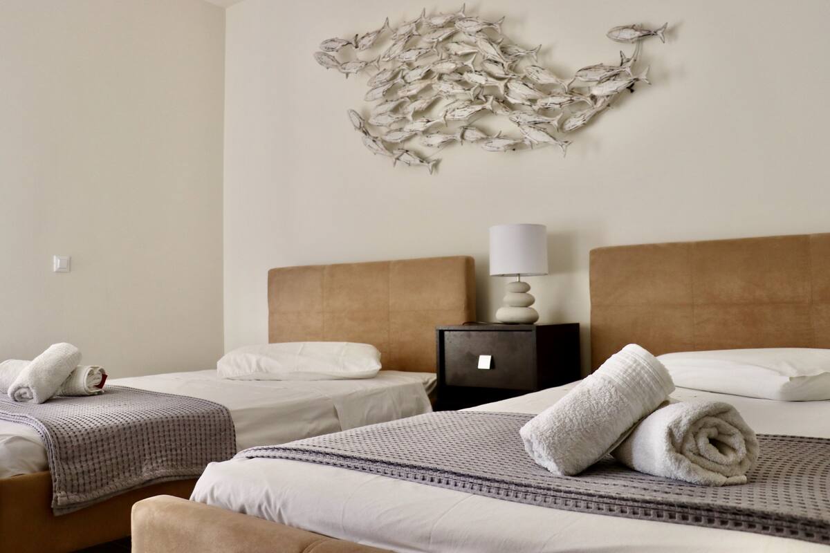 A hotel room with two beds, a wall art of fish, a bedside table with a lamp, and neatly made towels.