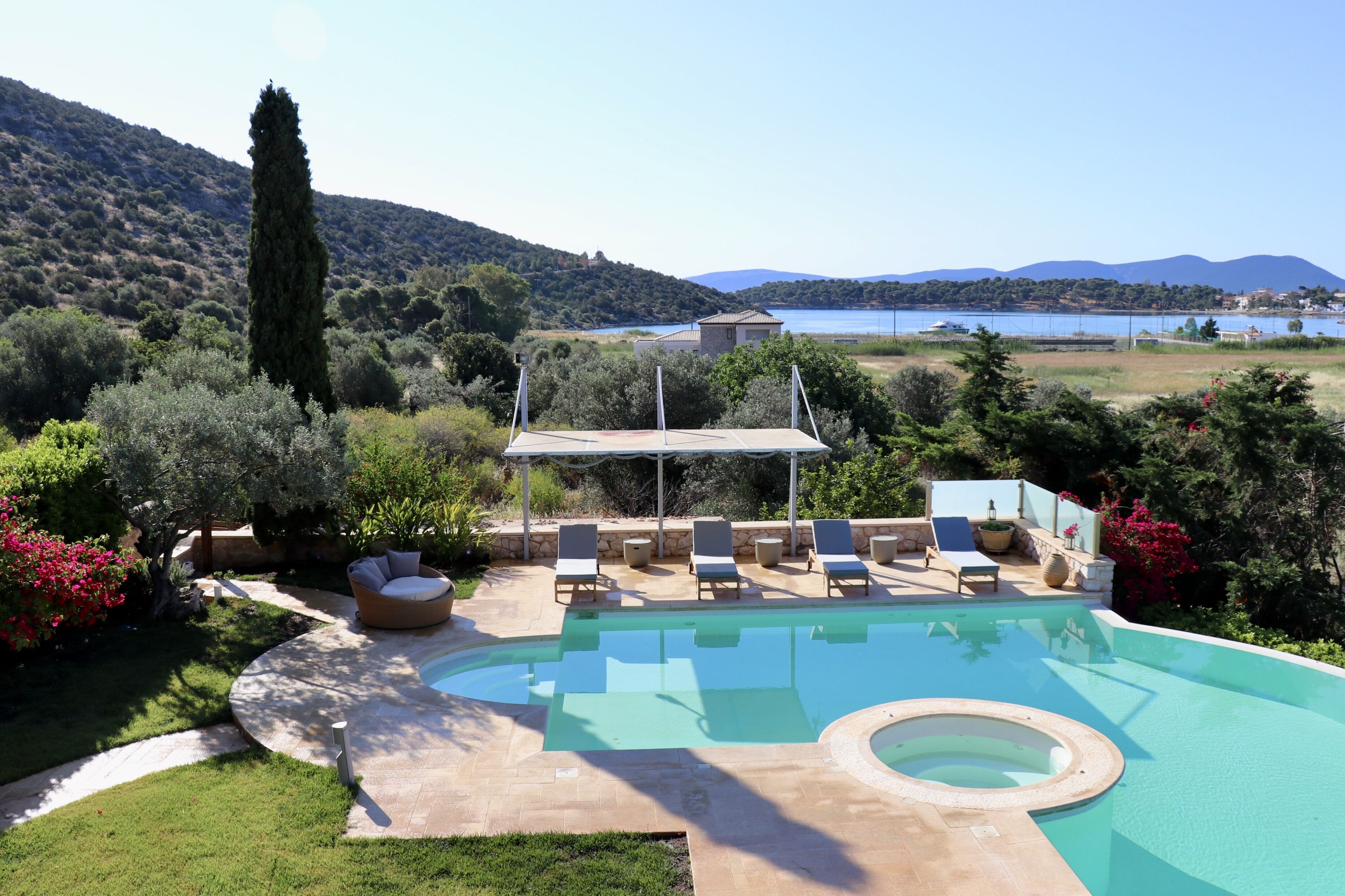 A pool area with lounge chairs, a covered seating area, and a view of a lake and hills.