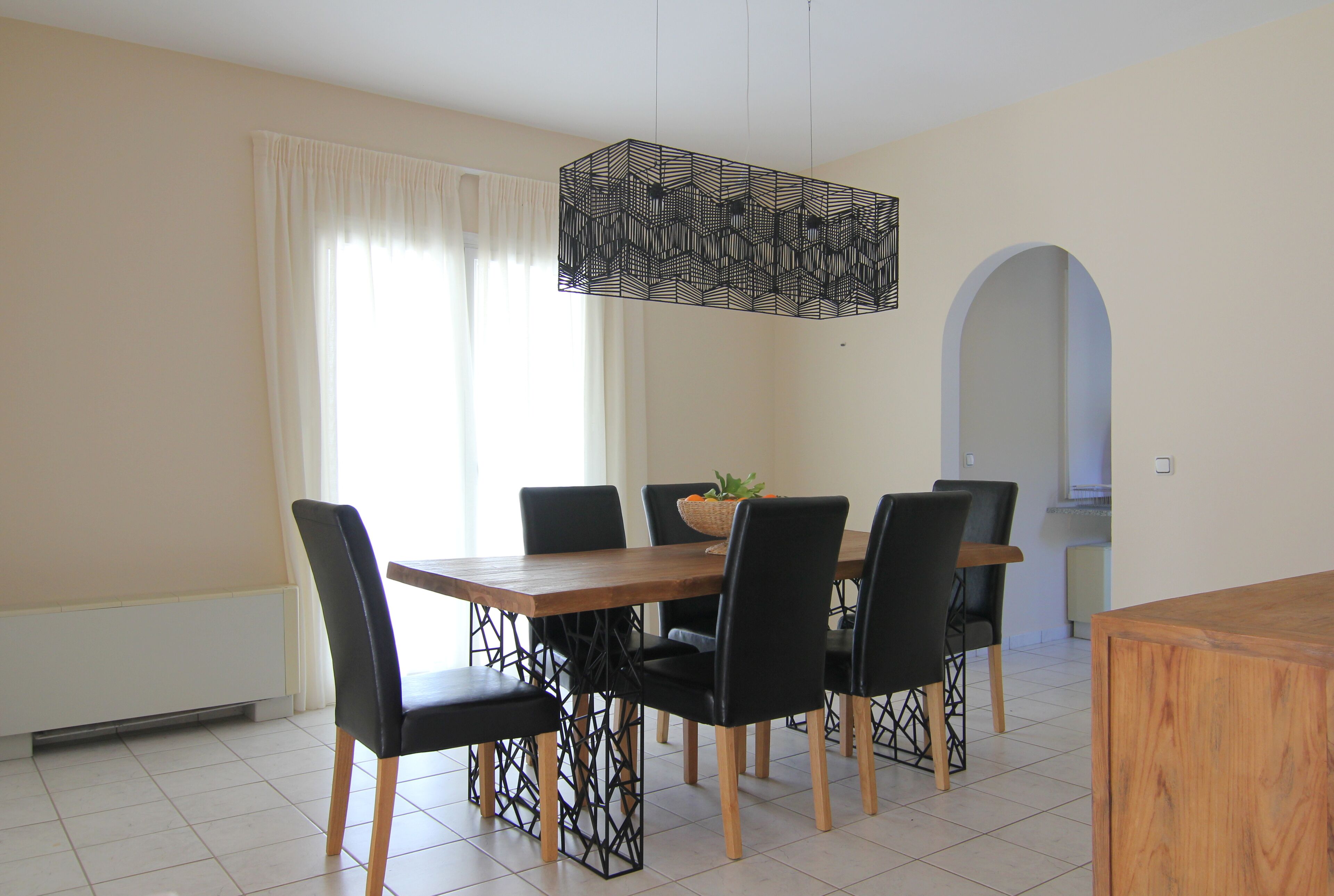 A dining area with a wooden table, black chairs, and a hanging light fixture.