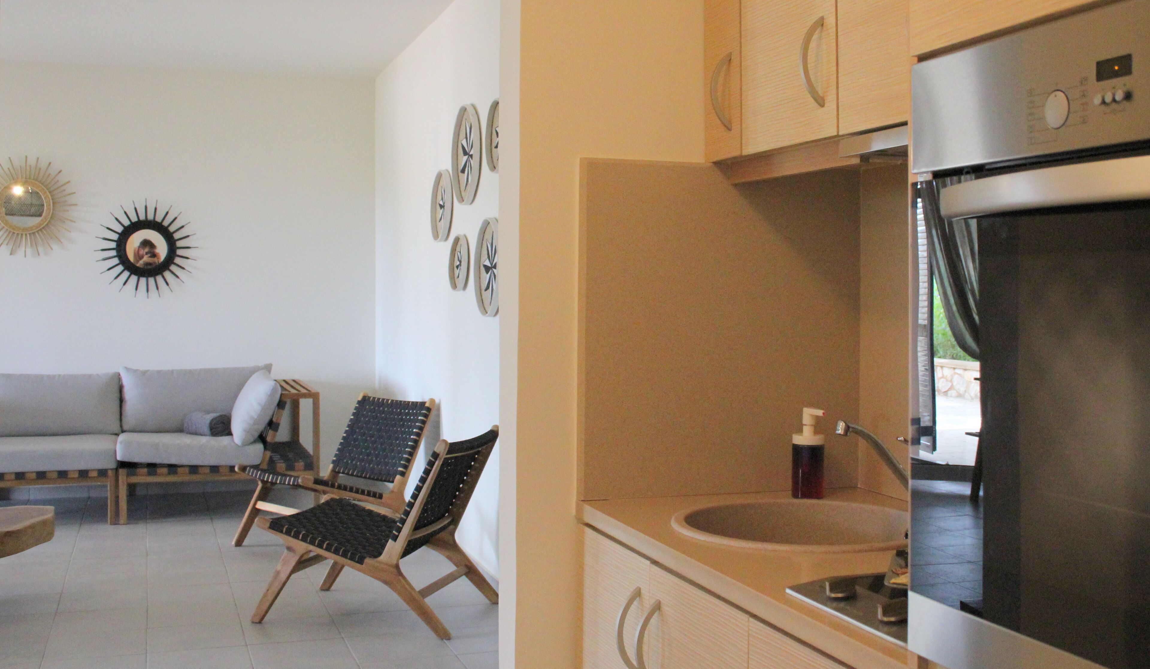 A modern kitchen with a built-in oven and sink, wooden cabinets, and a dining area with a sofa and two chairs.