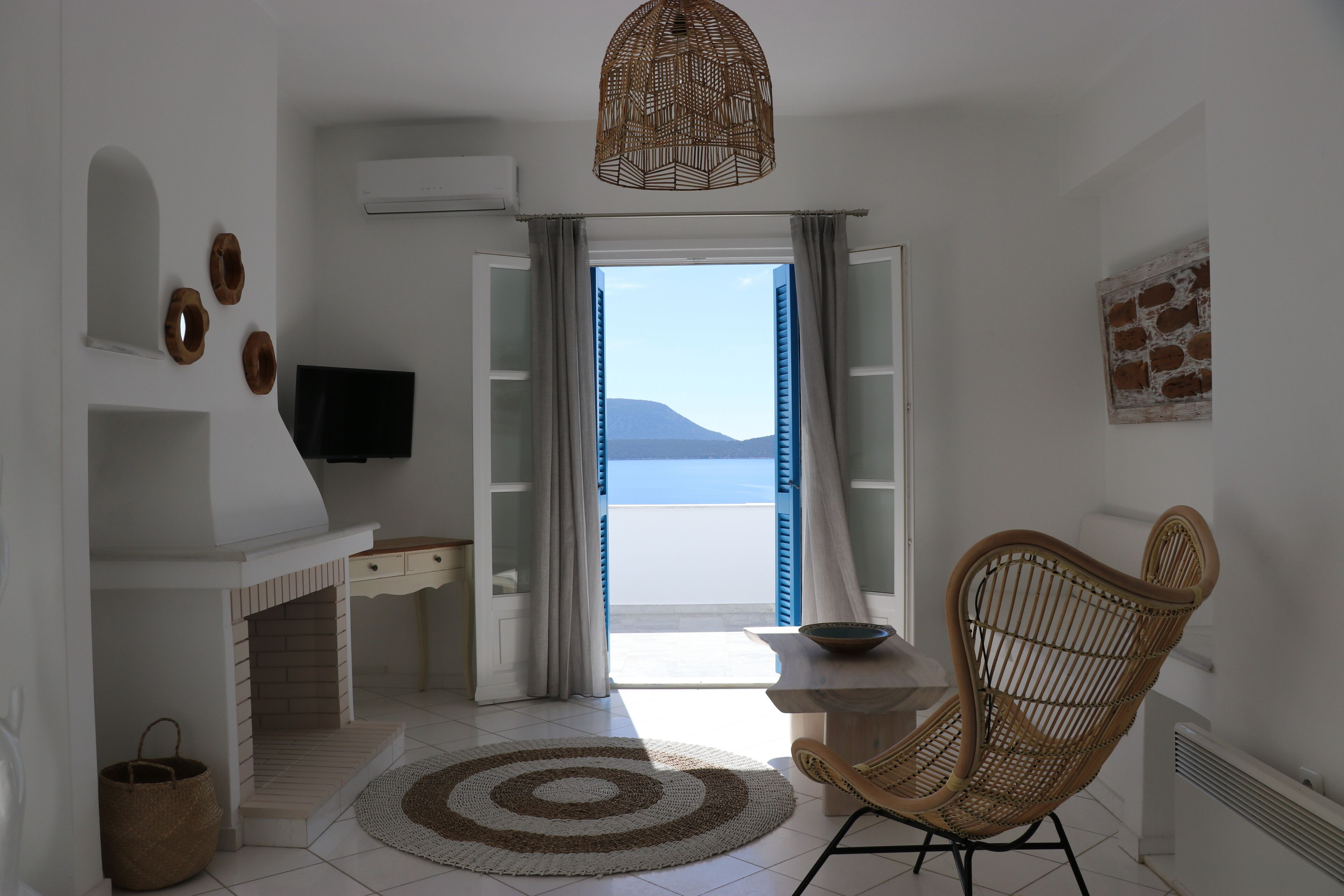 A room with a view of the sea, a wicker chair, a television, and a small table.