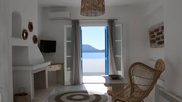 A room with a view of the sea, a wicker chair, a television, and a small table.