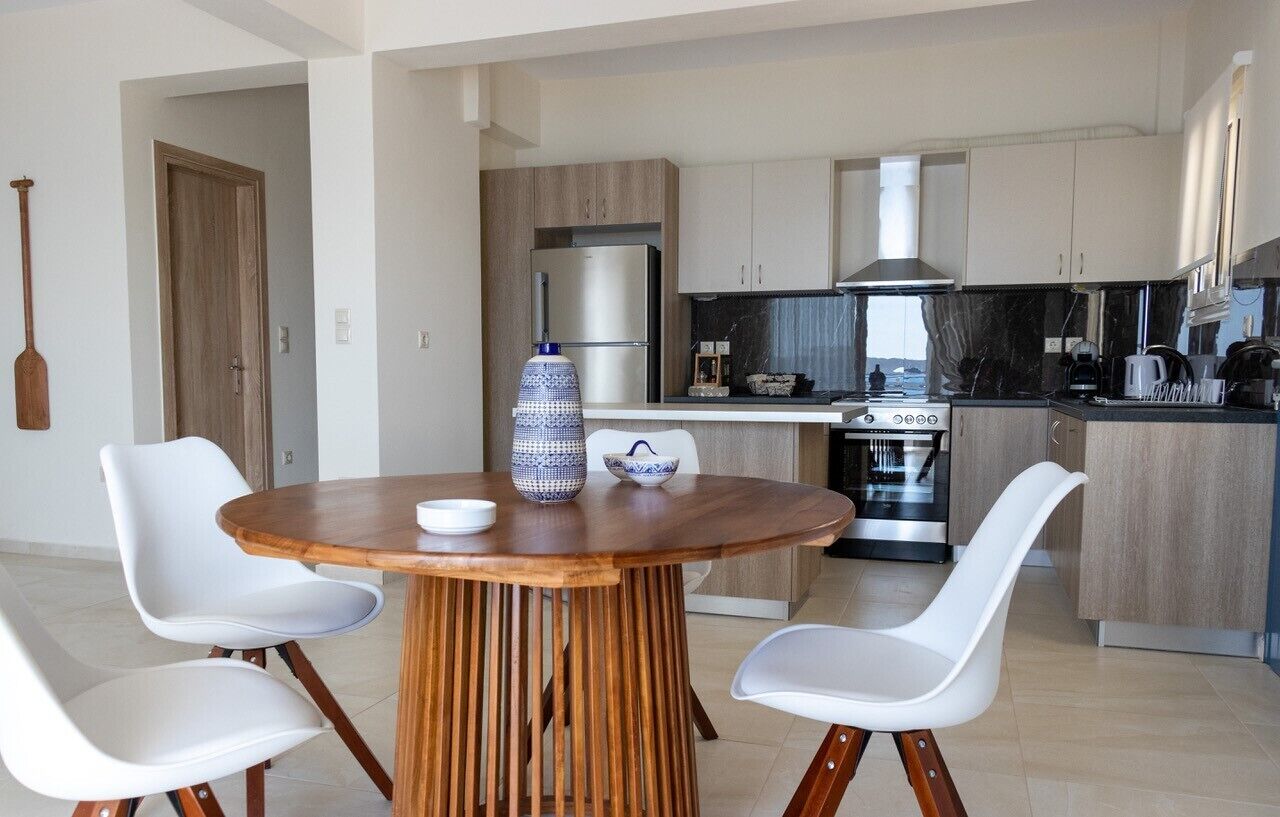 A modern kitchen with a central island, white chairs, and a wooden table.