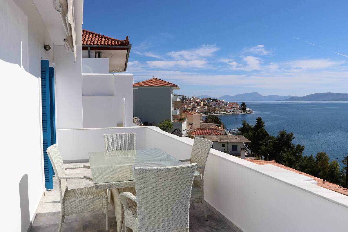 A balcony with wicker furniture overlooking a coastal town and the sea.