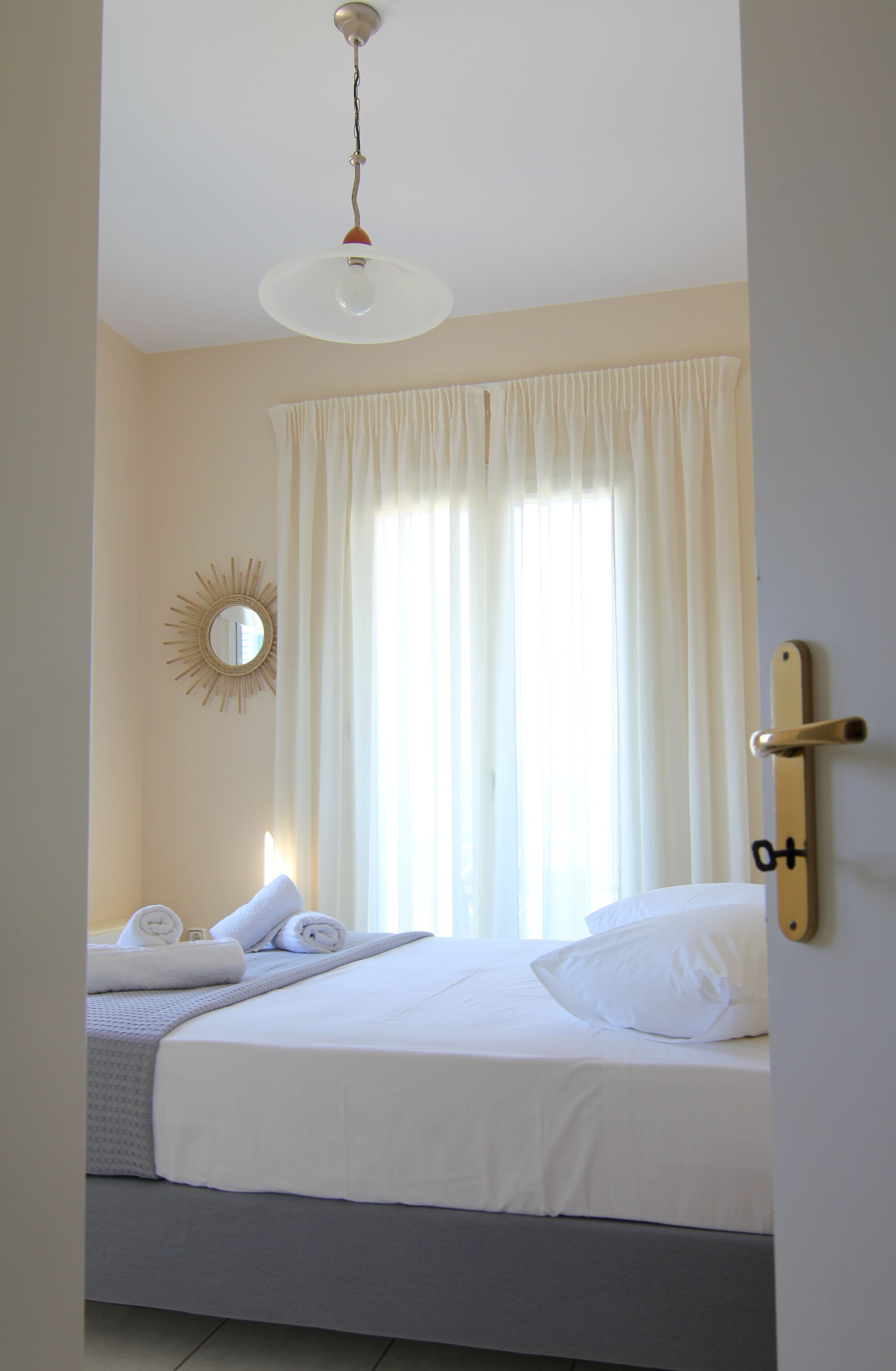 Un lit bien fait, avec du linge de lit blanc, une table de chevet avec une lampe et une fenêtre avec des rideaux.