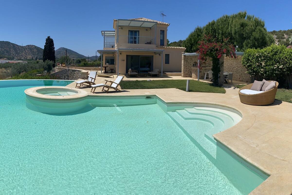 A swimming pool with lounge chairs, a stone house, and a view of mountains.