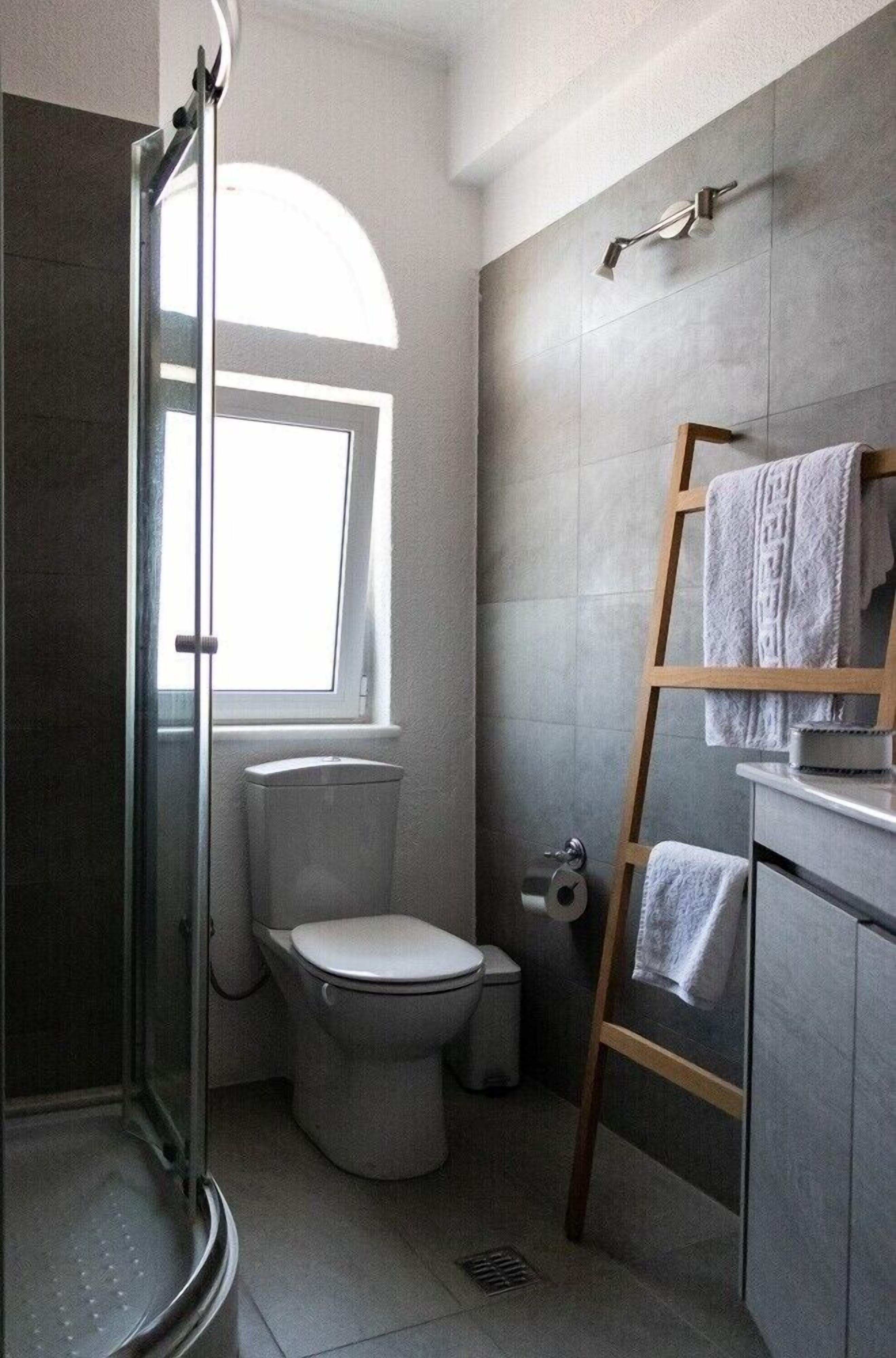 Un baño moderno con cabina de ducha de vidrio, inodoro, ventana y toallero.