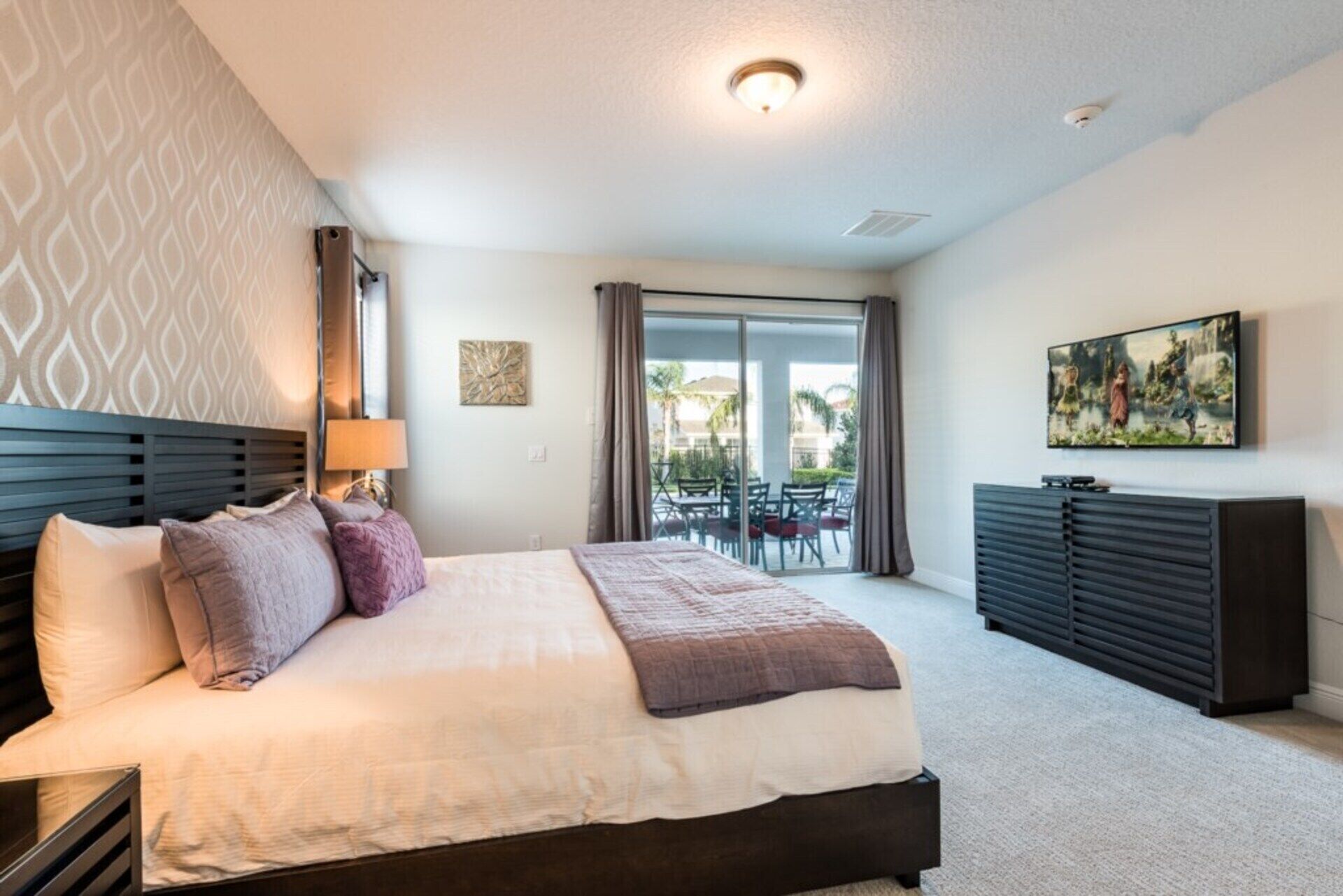 A modern hotel room with a large bed, a desk, and a balcony with outdoor furniture.