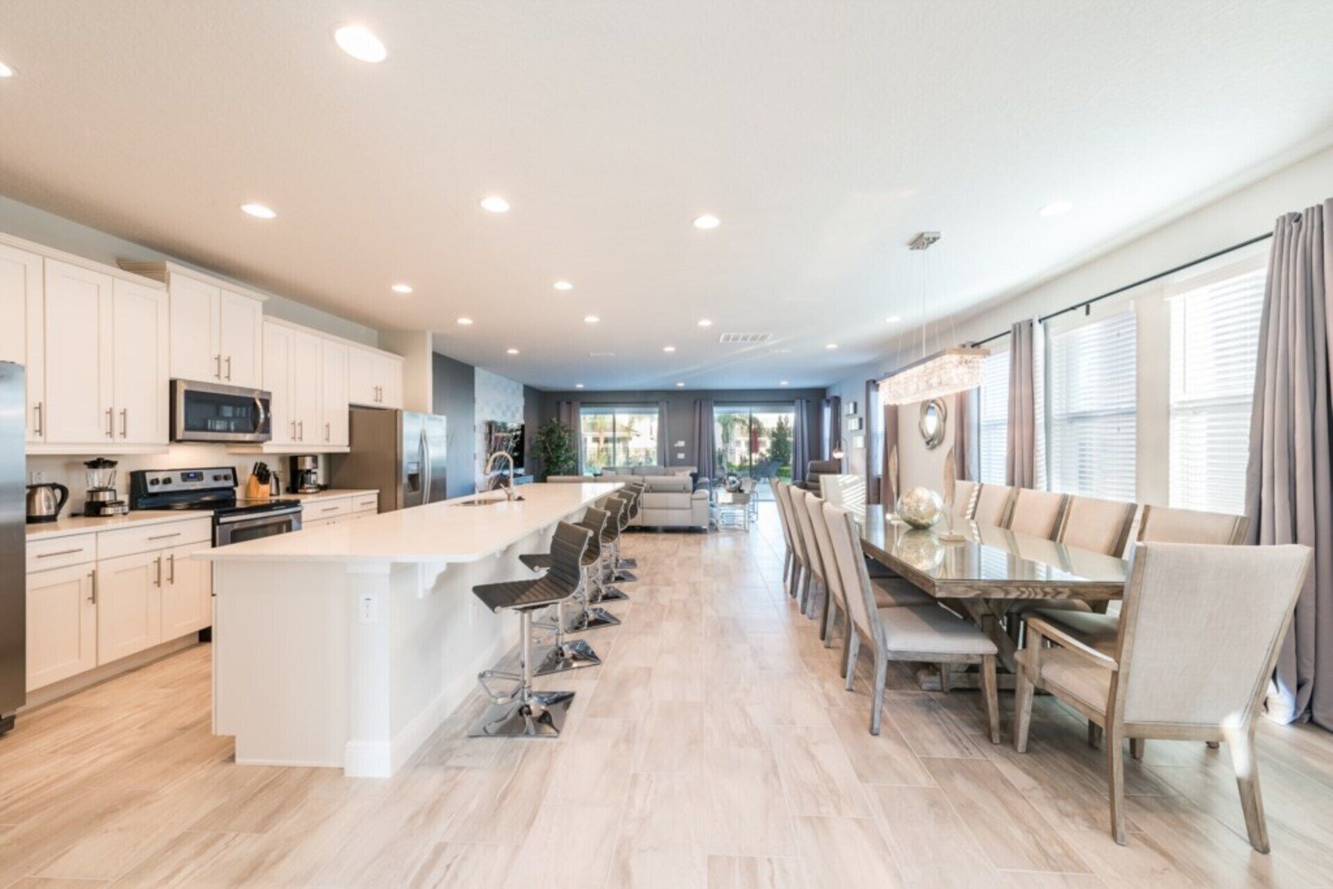 A modern kitchen with a central island, a dining area with a long table, and a view of the outdoors through large windows.