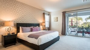 A hotel room with a large bed, a nightstand, a wall with a geometric pattern, a ceiling light, and a view of an outdoor patio with chairs and a table.