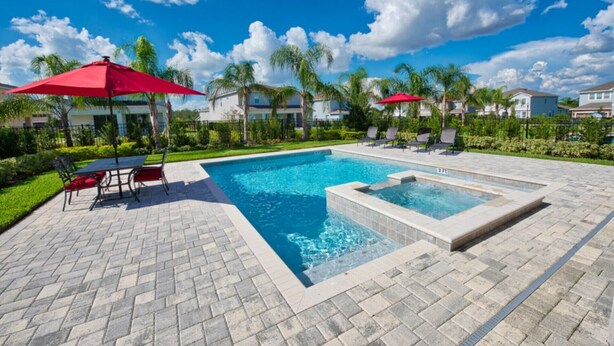 A swimming pool with a tiled deck, red umbrellas, and lounge chairs.