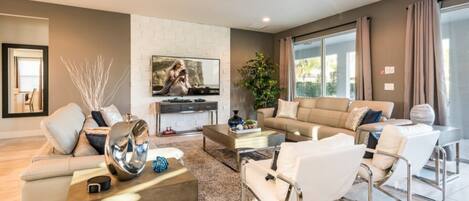 A modern living room with a sofa, coffee table, and chairs. There is a TV mounted on the wall and a plant in the corner.