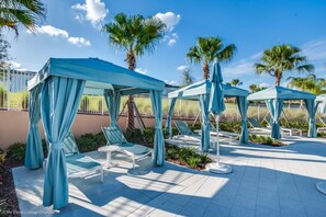 A poolside area with blue canopies, lounge chairs, and palm trees. - Villa Close to Disney, Orlando Villa 2615 (Kissimmee)