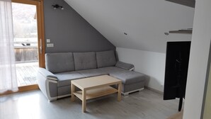 Un dormitorio tipo loft moderno con un sofá seccional gris, una mesa de centro de madera y una puerta corrediza que da a un balcón.