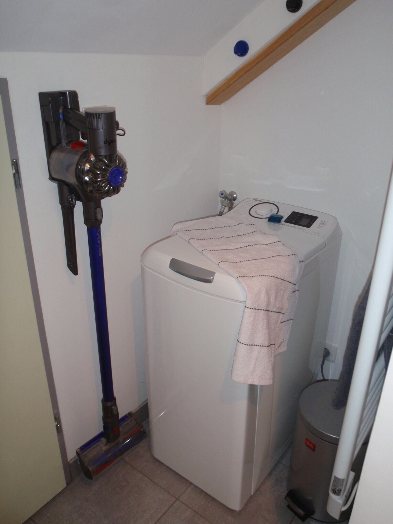 Uma lavanderia compacta com máquina de lavar, secadora e aspirador de pó.