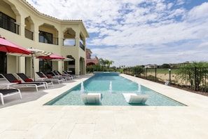 A swimming pool with lounge chairs and umbrellas, surrounded by a fence and a building with balconies. - Beautiful Mansion With Private Pool, Close to Disney, Orlando Mansion 1574 (Kissimmee)