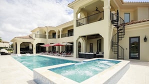 A large outdoor swimming pool with a hot tub, surrounded by lounge chairs and umbrellas, and a multi-story building with balconies and a spiral staircase. - Beautiful Mansion With Private Pool, Close to Disney, Orlando Mansion 1574 (Kissimmee)