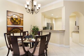 A dining area with a round table, six chairs, a chandelier, and a painting on the wall.