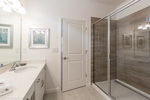 A bathroom with a white vanity, a glass shower enclosure, and two framed pictures on the wall.
