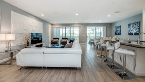 A spacious living area with a white sofa, a dining area with bar stools, and a kitchen with a bar counter. - Beautiful Villa With Private Pool, Close to Disney, Orlando Villa 2657 (Kissimmee)