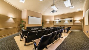 A conference room with rows of chairs, a projector screen, and wall-mounted lighting.