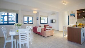A spacious living area with a dining table, white chairs, a red sofa, and a kitchen area with a counter and appliances. - Beautiful Villa With Private Pool, Pernera Villa 1004 (Paralimni)