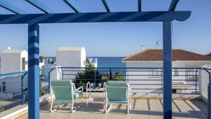 A terrace with two green chairs and a table, overlooking a coastal view with buildings and the sea. - Beautiful Villa With Private Pool, Pernera Villa 1004 (Paralimni)
