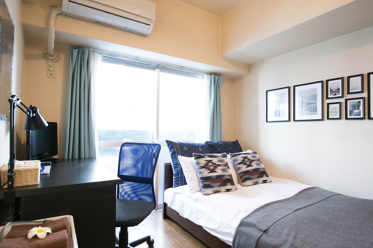 Habitació d'hotel amb un llit, una escriptori amb un ordinador, una cadira i una finestra amb cortines.