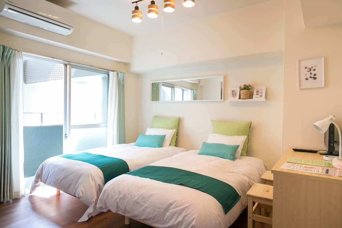 Habitació d'hotel amb dos llits, una taula amb una làmpada, un ordinador i una finestra amb cortines.