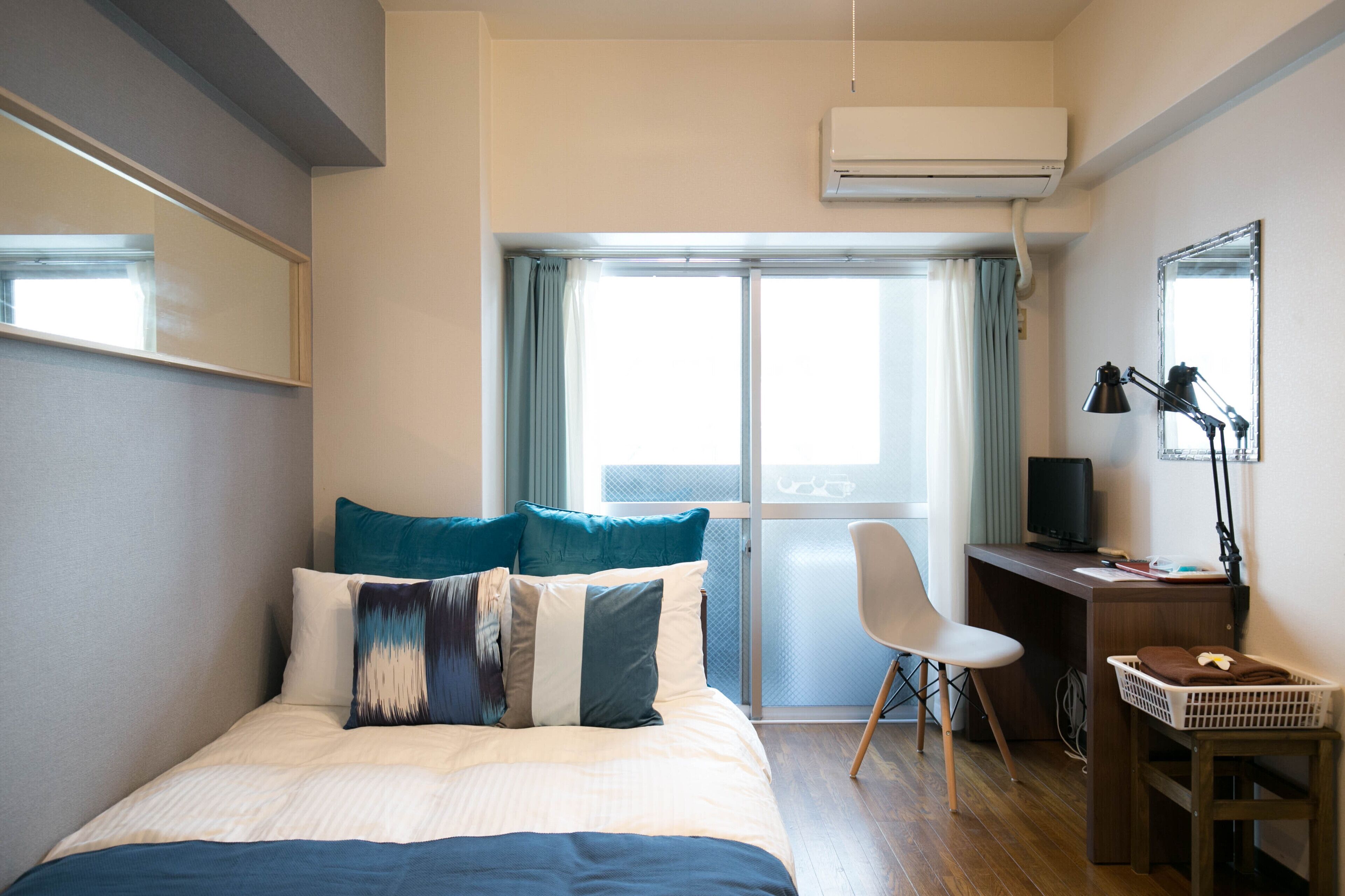 Una habitación de hotel con cama, escritorio, silla, televisor y ventana con cortinas.