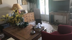 A living room with a wooden coffee table, a red armchair, a TV, and a window with curtains. - VILLA WITH POOL, PANORAMIC VIEW, 5 MINUTES WALK FROM THE VILLAGE (Lorgues)