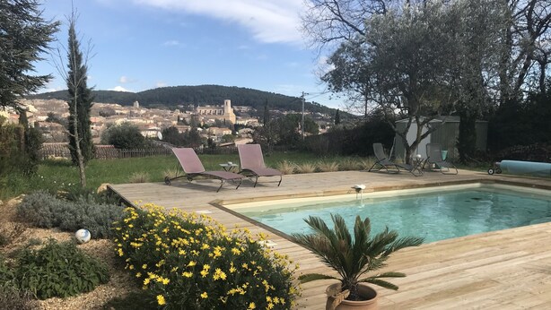 A pool area with lounge chairs, a potted plant, and a view of a town in the background. - VILLA WITH POOL, PANORAMIC VIEW, 5 MINUTES WALK FROM THE VILLAGE (Lorgues)