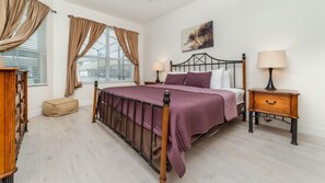 A bedroom with a bed, two bedside tables, a window with curtains, a painting on the wall, and a wooden dresser. - Luxury 5 Bedroom Villa on Windsor Hills Resort, Orlando Villa 3368 (Kissimmee)
