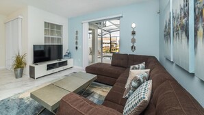A living room with a brown sofa, a flat-screen TV, and a large window. - Rent a Luxury Townhome on Storey Lake Resort, Minutes From Disney, Orlando Townhome 1004 (Kissimmee)